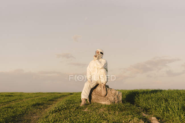 Hombre con traje protector y máscara sentado en una roca en el campo - foto de stock