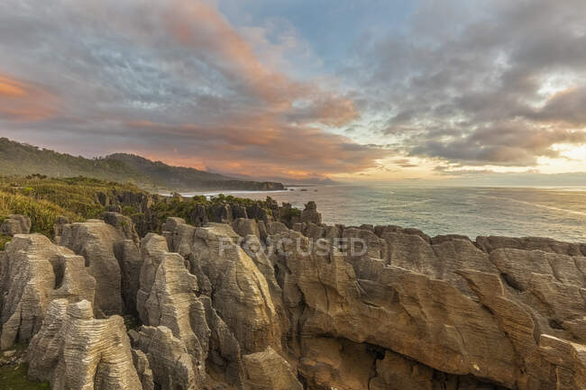 Nouvelle-Zélande, district Buller, Punakaiki, formation de roches calcaires à crêpes et trou de soufflage côtier au crépuscule — Photo de stock