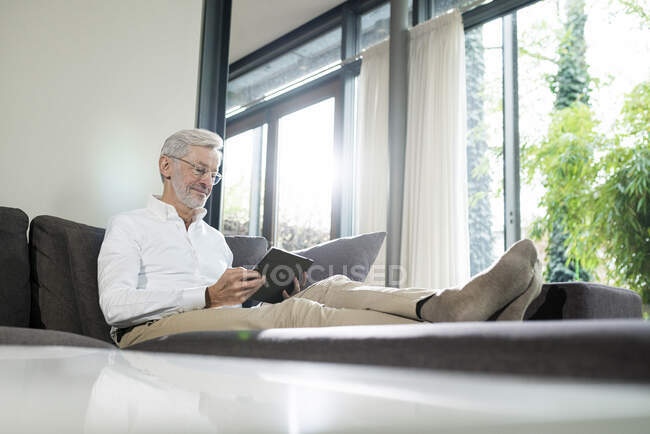 Älterer Mann mit grauen Haaren in modernem Design Wohnzimmer sitzt auf Couch mit Tablet — Stockfoto