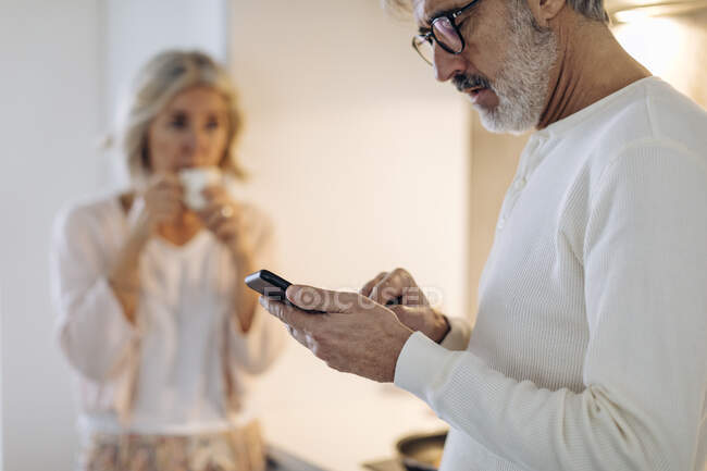 Домашній дорослий чоловік з дружиною користується мобільним телефоном. — стокове фото