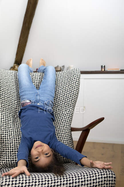 Retrato de menina pendurada de cabeça para baixo do encosto de uma poltrona — Fotografia de Stock