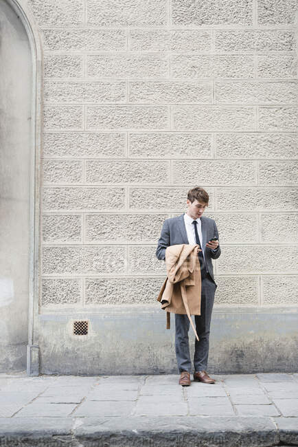 Young businessman standing on pavement looking at smartphone — Stock Photo