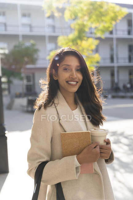 Portrait of smiling young woman with book and takeaway coffee in the city — Stock Photo