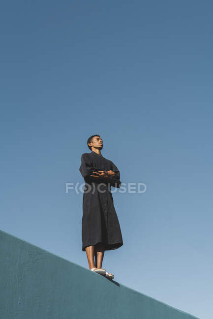 Молодой человек в черном кафтане стоит на синей стене — стоковое фото