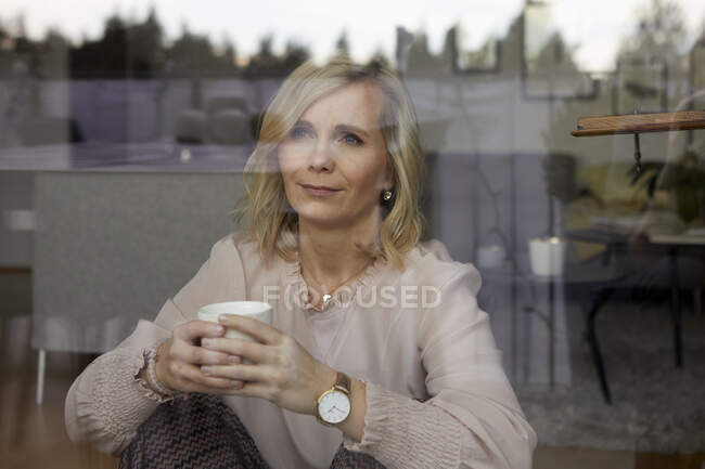 Retrato de mujer rubia detrás del cristal de la ventana en casa - foto de stock