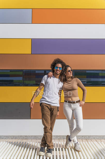 Улыбающаяся пара, стоящая перед красочной стеной, с обхваченными руками — стоковое фото