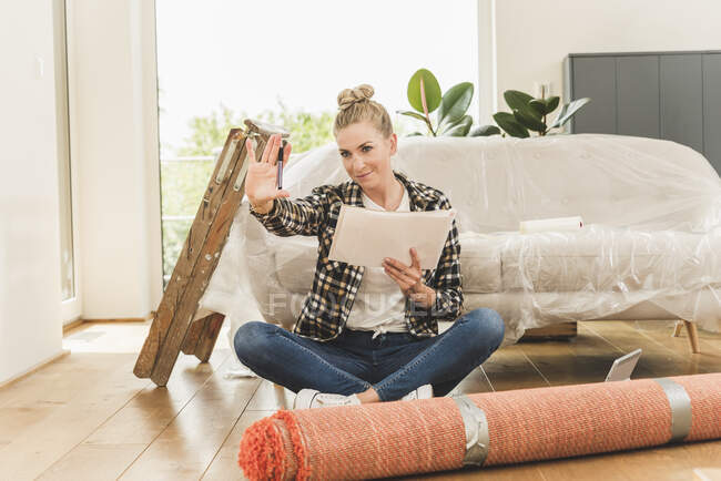 Donna seduta sul pavimento in una nuova casa alzando la mano — Foto stock