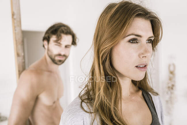 Retrato de mujer joven seria en el dormitorio con el hombre en el fondo - foto de stock
