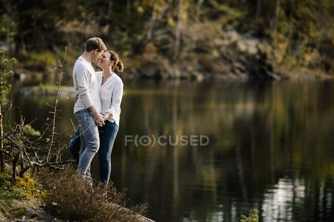 Couple affectueux debout sur un rocher au bord du lac, Forstsee, Carinthie, Autriche — Photo de stock