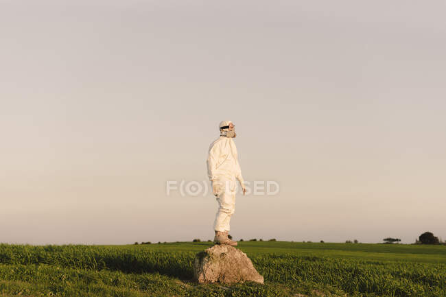 Hombre con traje protector y máscara de pie sobre una roca en el campo - foto de stock
