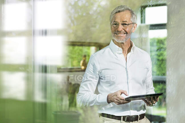 Lächelnder älterer Mann mit grauen Haaren in modern gestaltetem Wohnzimmer mit Tablet — Stockfoto