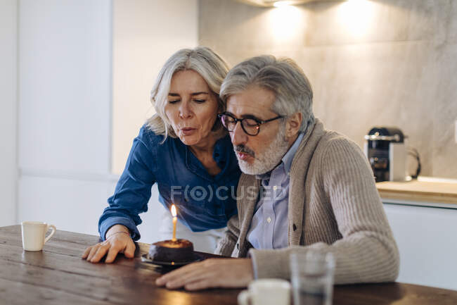 Mature couple celebrating birthday with cake in kitchen at home — Stock Photo