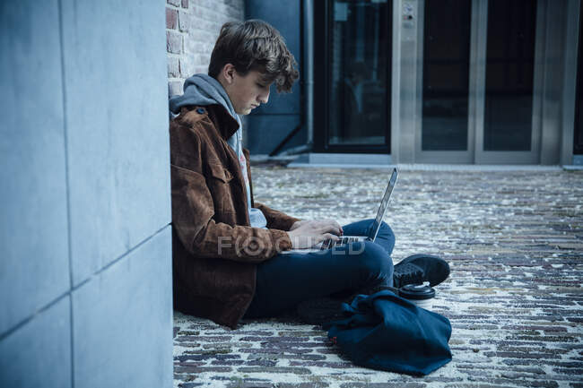Мбаппе использует ноутбук и сидит на каменном полу в городе — стоковое фото