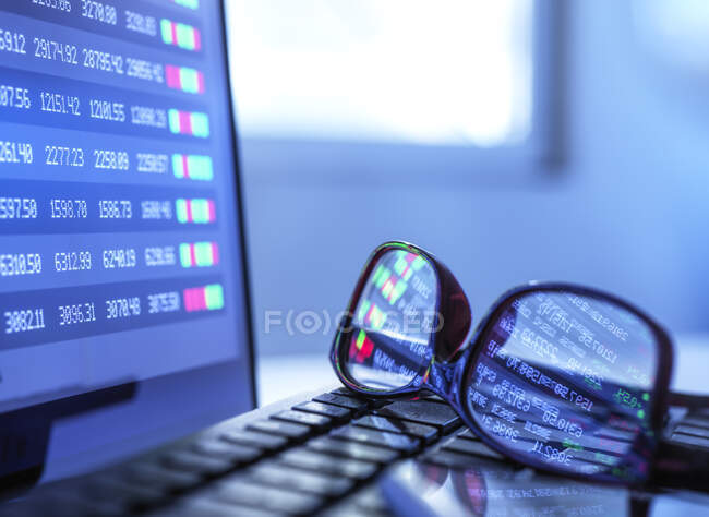 Dati di borsa che riflettono in occhiali sdraiati sulla tastiera del computer portatile — Foto stock