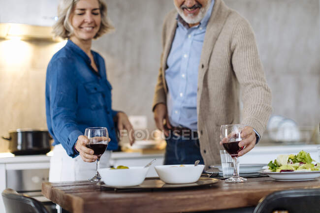 Зріла пара виховує келихи під час вечері на кухні вдома — стокове фото