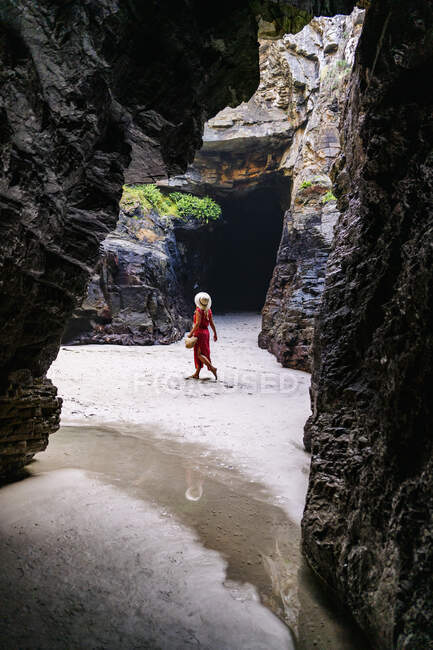 Donna bionda vestita di rosso e cappello in una grotta rocciosa, Playa de Las Catedrales, Spagna — Foto stock