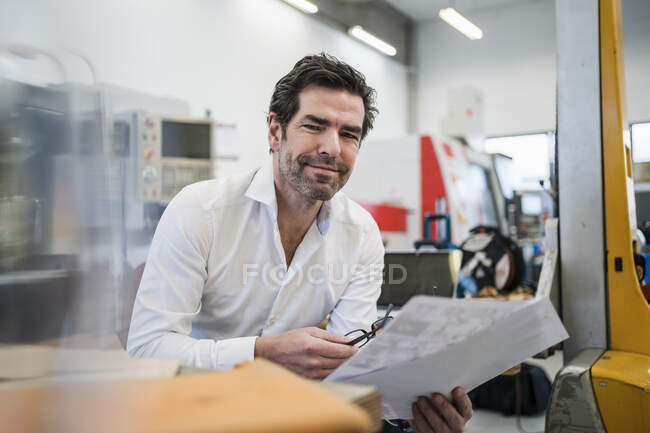 Porträt eines selbstbewussten Geschäftsmannes mit Papieren in einer Fabrik — Stockfoto