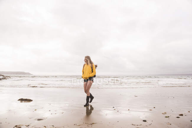 Жінка в жовтій куртці, що йде на пляжі. — стокове фото
