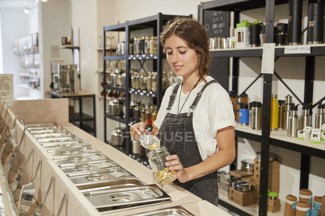 Молодая женщина в супермаркете без упаковки наполняет макароны в банку — стоковое фото