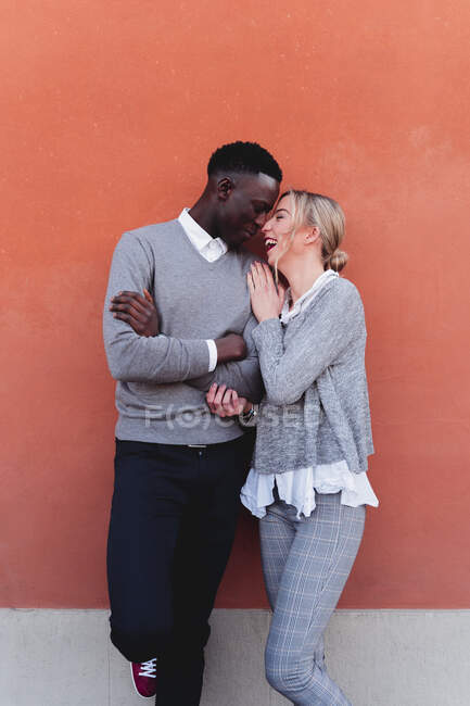Heureux jeune couple affectueux debout à un mur orange — Photo de stock