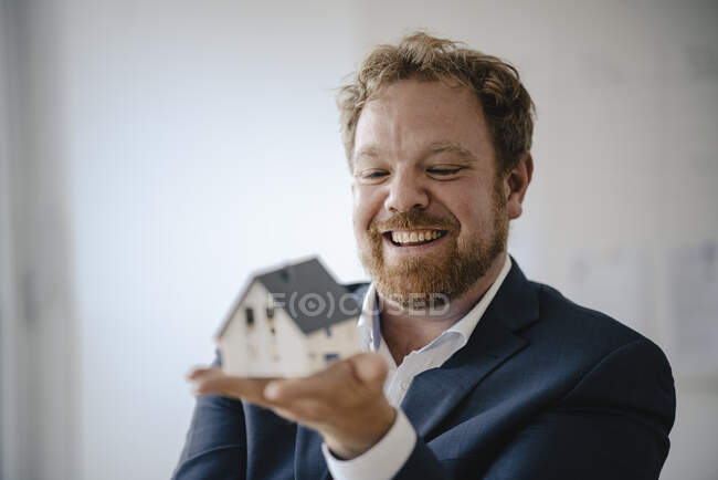 Happy businessman holding model house in office — Stock Photo