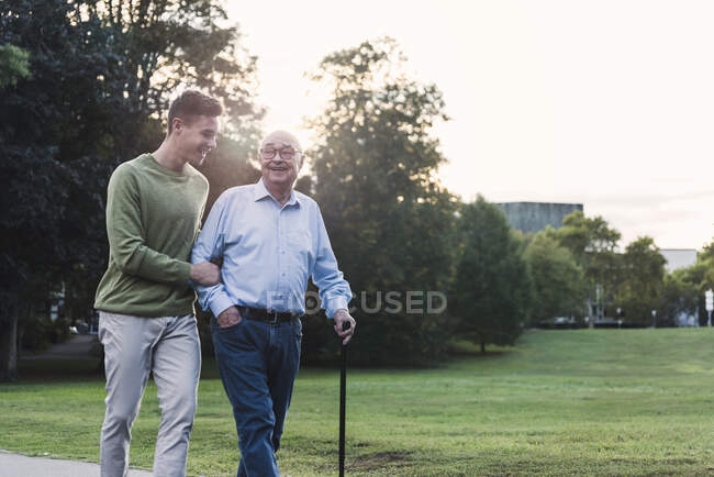 Young man assisting his grandfather walking in a park — Stock Photo