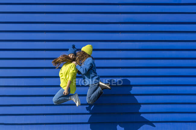 Due adolescenti che indossano vestiti coordinati che saltano in aria di fronte a sfondo blu — Foto stock