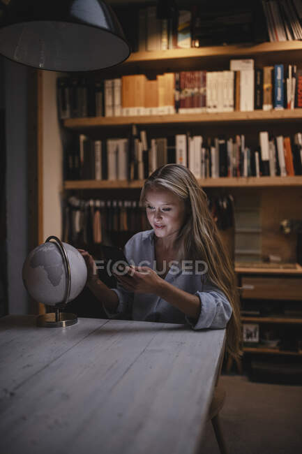 Jovem mulher sentada à mesa com smartphone e globo — Fotografia de Stock