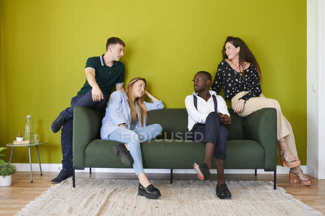 Colegas casuales hablando en un sofá en un salón de oficinas con paredes verdes - foto de stock