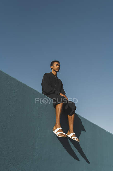Молодой человек в черном кафтане сидит на голубой стене — стоковое фото