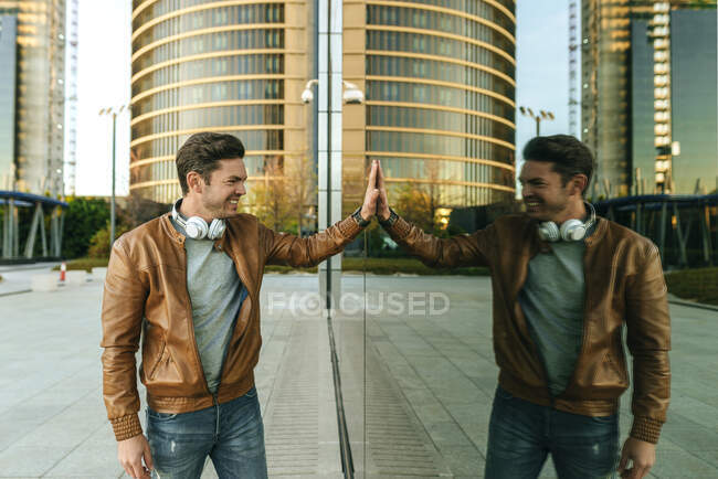 Lächelnder Mann, der sein Spiegelbild in der Glasscheibe eines städtischen Gebäudes betrachtet, Madrid, Spanien — Stockfoto