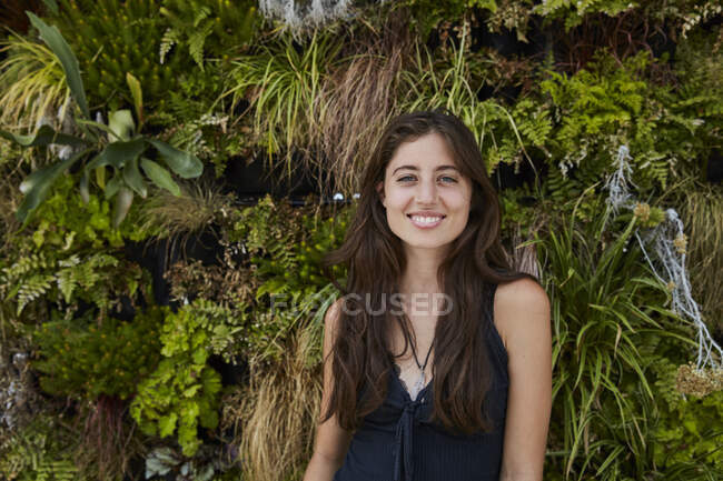 Porträt einer lächelnden jungen Frau vor einer Pflanzenmauer — Stockfoto