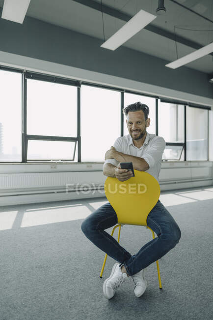 Ritratto di uomo d'affari maturo e sicuro seduto su una sedia gialla in un ufficio vuoto — Foto stock