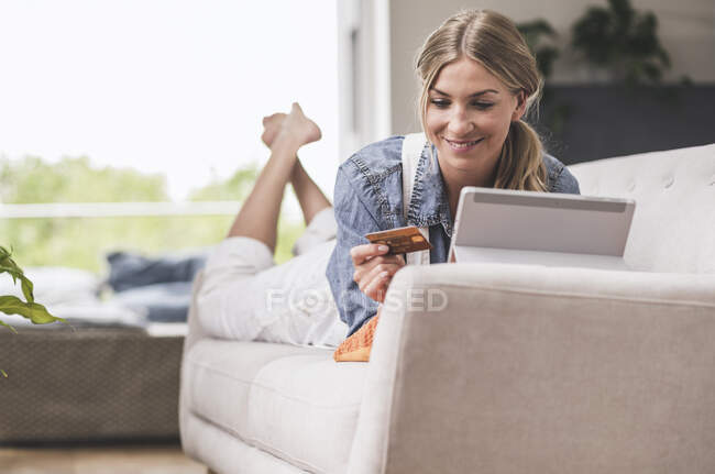 Mulher sorridente no sofá com cartão de crédito e tablet — Fotografia de Stock