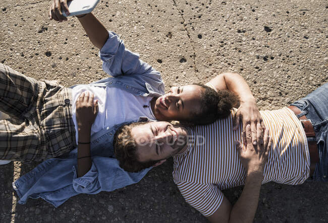 Glückliches junges Paar liegt auf Betonboden und macht ein Selfie — Stockfoto