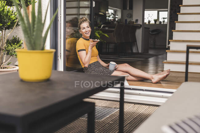 Розслаблена жінка сидить вдома на терасі за допомогою смартфона. — стокове фото