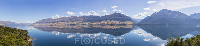 Новая Зеландия, район Куинстаун-Лейкс, Ванака, озеро Ванака, отражающее голубое летнее небо и окружающие холмы — стоковое фото