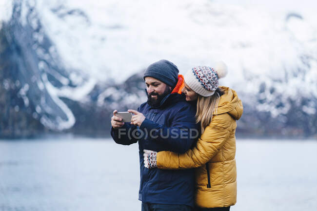Туристическая пара со смартфоном в Hamnoy, Лофотене, Норвегия — стоковое фото