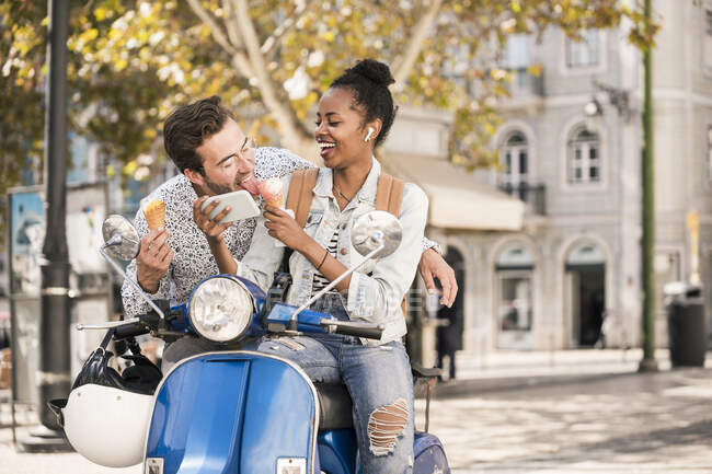 Jovem casal feliz com scooter de motor, sorvete e telefone celular na cidade, Lisboa, Portugal — Fotografia de Stock