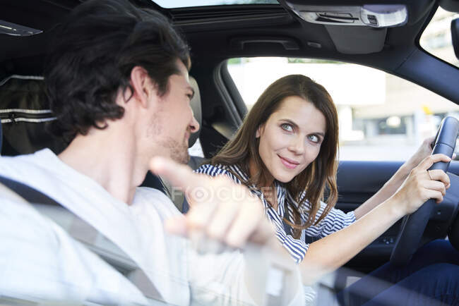 Couple heureux dans une voiture avec la femme au volant et l'homme pointant son doigt — Photo de stock