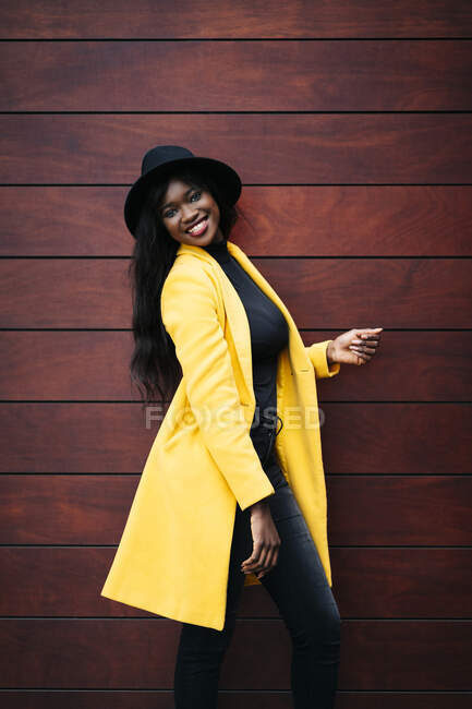 Портрет улыбающейся модной молодой женщины, позирующей у деревянной стены — стоковое фото