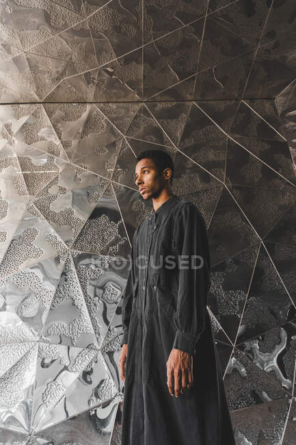 Молодий чоловік у чорному кафтані стоїть біля стіни. — стокове фото
