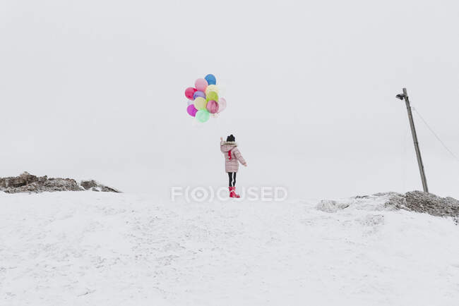 Вид сзади девушки с шариками, стоящей зимой на заснеженном холме — стоковое фото