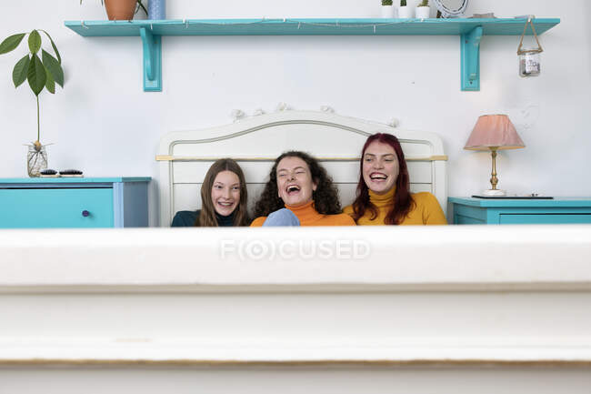 Портрет трех смеющихся сестер, сидящих бок о бок на кровати — стоковое фото