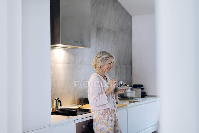 Mujer madura sosteniendo un plato con panqueques en la cocina en casa - foto de stock