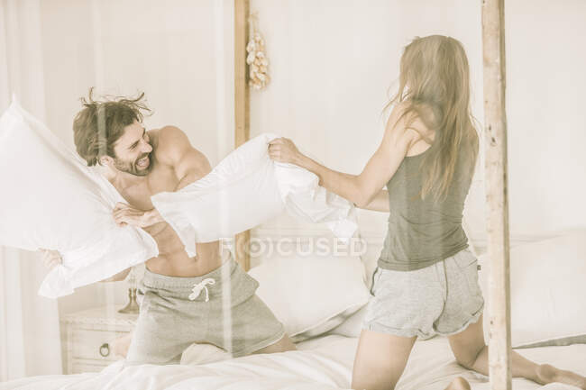 Carefree young couple having a pillow fight in bed — Stock Photo