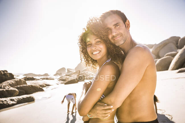 Couple heureux étreignant sur la plage avec des enfants en arrière-plan — Photo de stock
