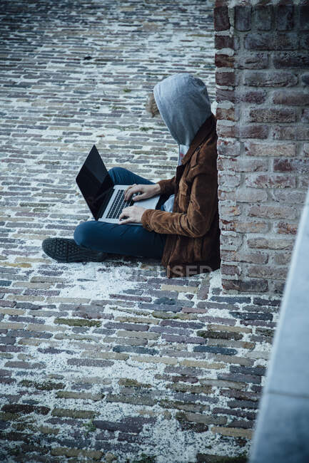 Teenager using laptop and sitting on a stone floor in the city — Stock Photo