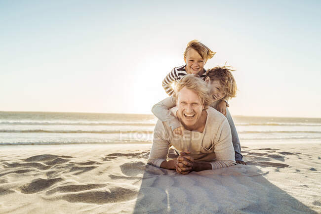 Father having fun with his son on the beach, lying in the sand on top of each other — Stock Photo