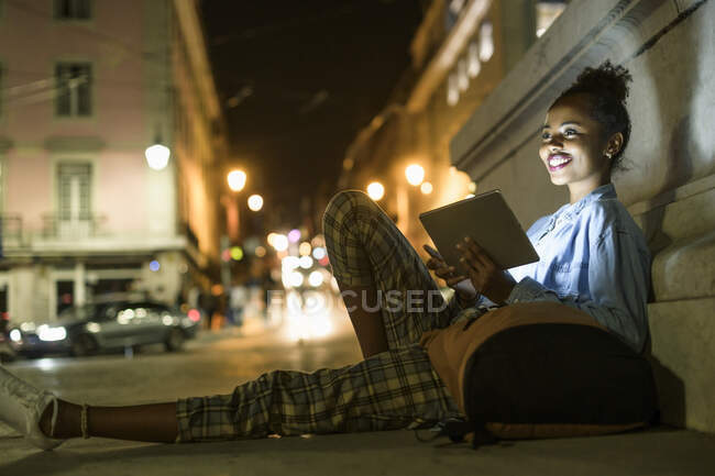 Portrait of happy young woman with  backpack and digital tablet in the city by night, Lisbon, Portugal — Stock Photo